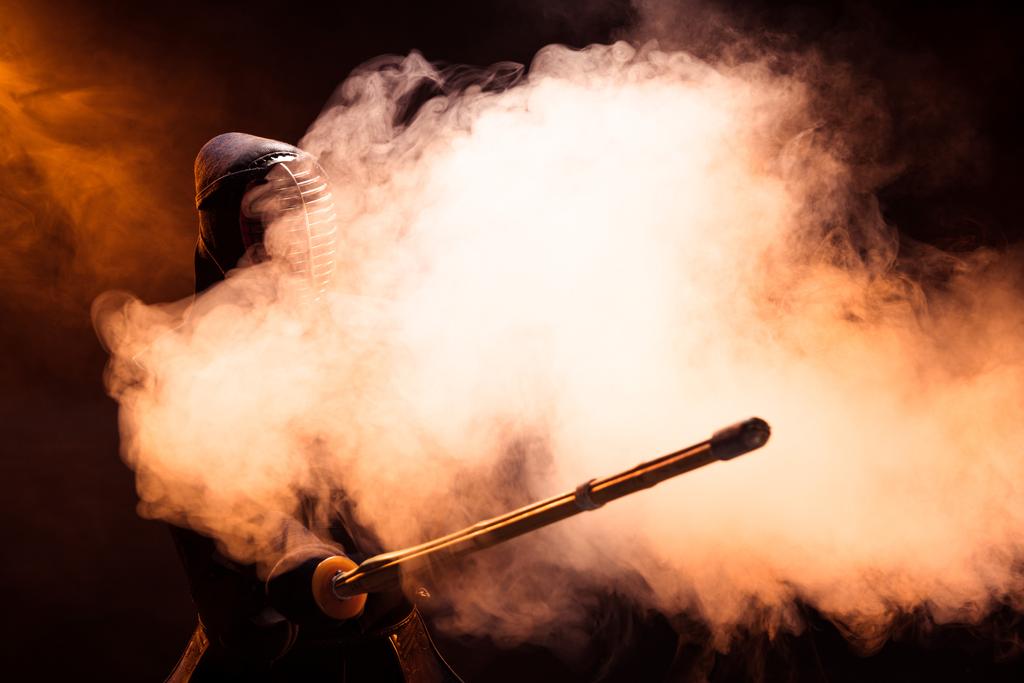 Kendo-Kämpfer im Helm hält Bambusschwert in Rauch - Foto, Bild