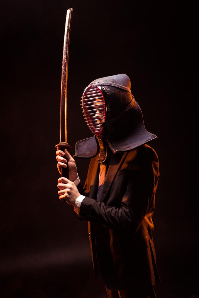 Kendo fighter in formal wear and helmet holding bamboo sword on dark - Photo, Image