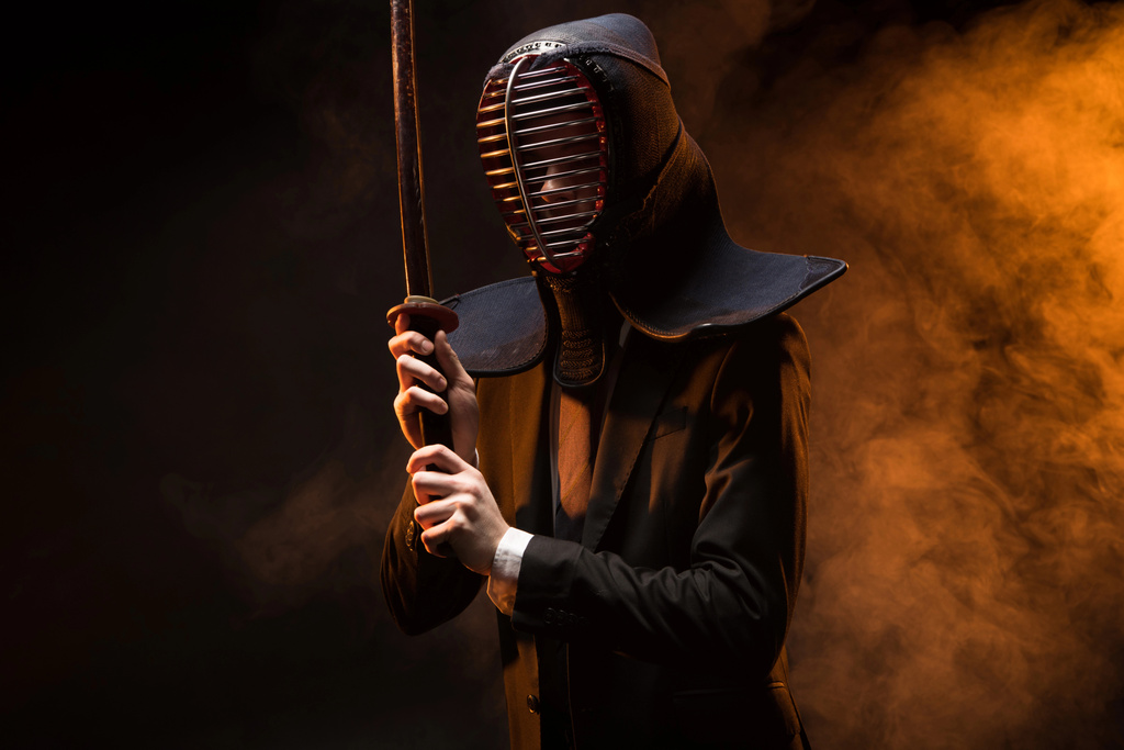 Kendo fighter in formal wear and helmet holding bamboo sword on dark - Photo, Image