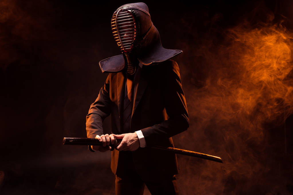 Combattant Kendo en tenue formelle et casque tenant épée de bambou sur sombre
 - Photo, image