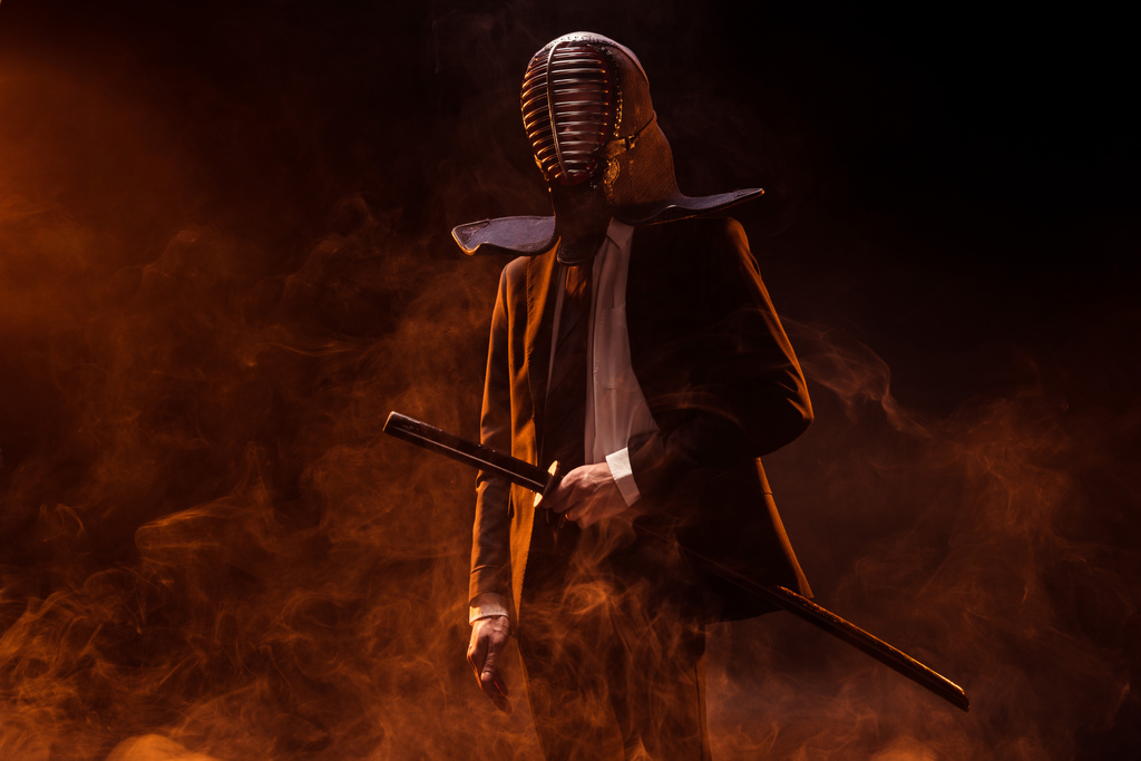Чоловік у формальному одязі та капелюсі, що тримає бамбуковий меч на темряві
 - Фото, зображення