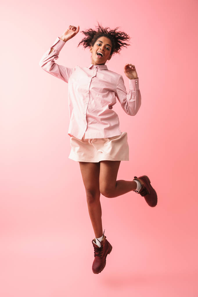 Hermosa joven africana posando aislada sobre fondo de pared rosa saltando
. - Foto, imagen