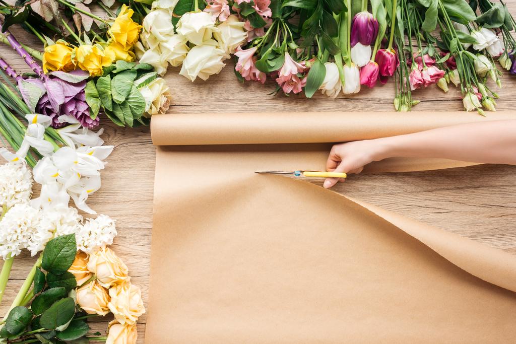 Vista parcial de papel artesanal de corte florista com tesoura perto de flores na superfície de madeira
 - Foto, Imagem