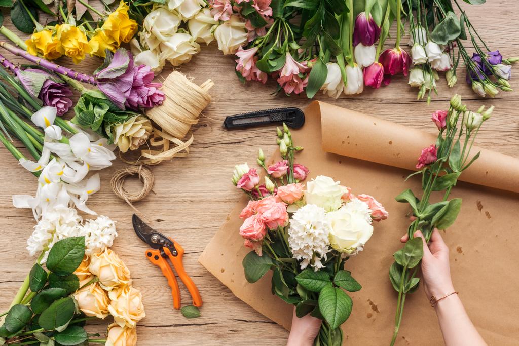 Partial view of florist making flower bouquet on wooden surface - Photo, Image