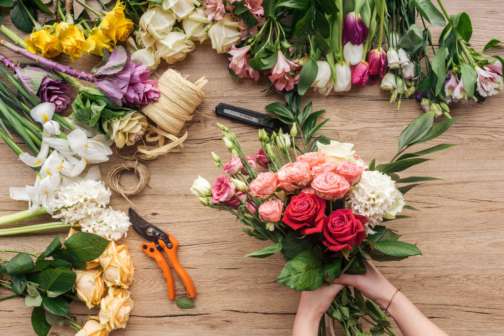Обрезанный вид флориста, держащего букет свежих цветов на деревянной поверхности
 - Фото, изображение