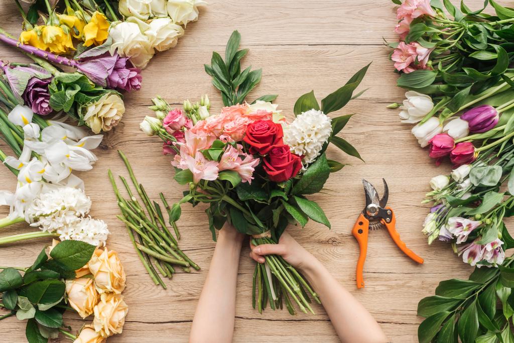 Vue recadrée du fleuriste tenant un bouquet de fleurs sur une table en bois
 - Photo, image