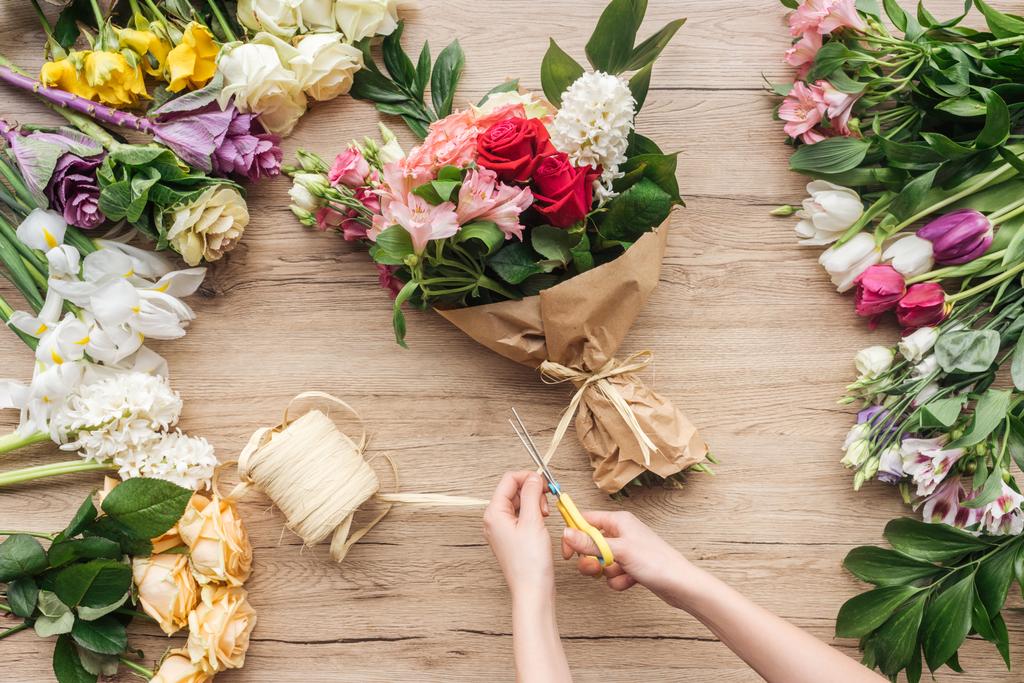 Vista ritagliata del fiorista che fa mazzo di fiori sulla superficie di legno
 - Foto, immagini