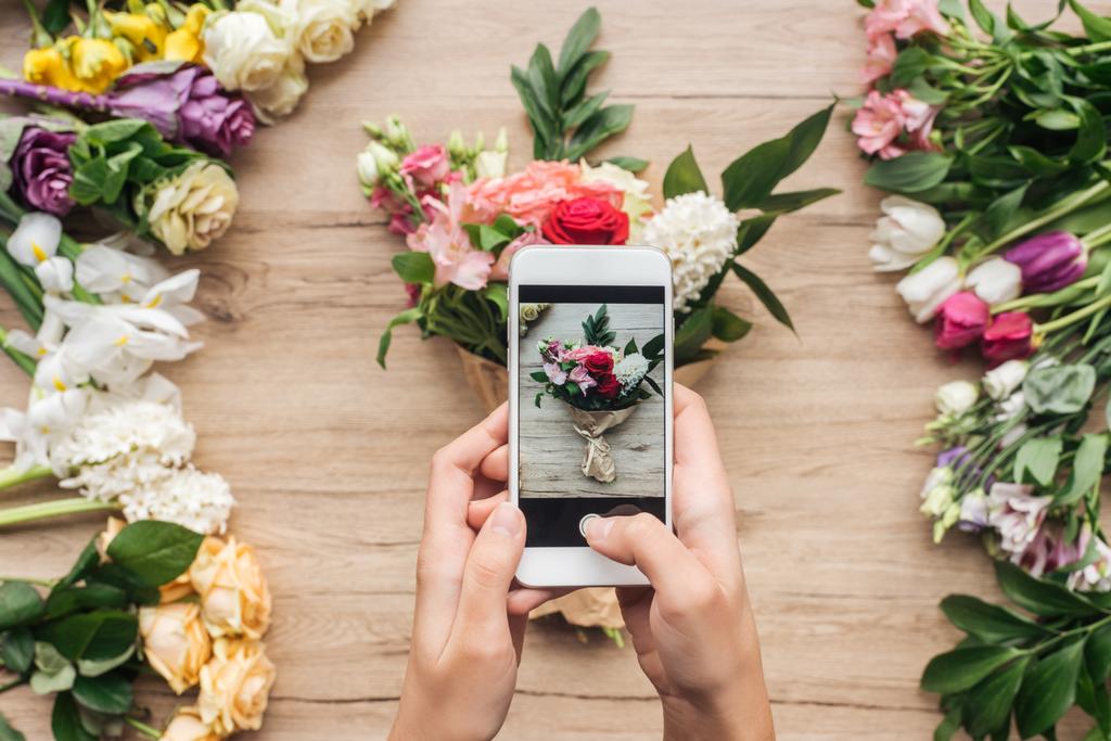 木の表面にスマート フォンと花の花束の写真を撮影を保持している花屋のビューをトリミング - 写真・画像