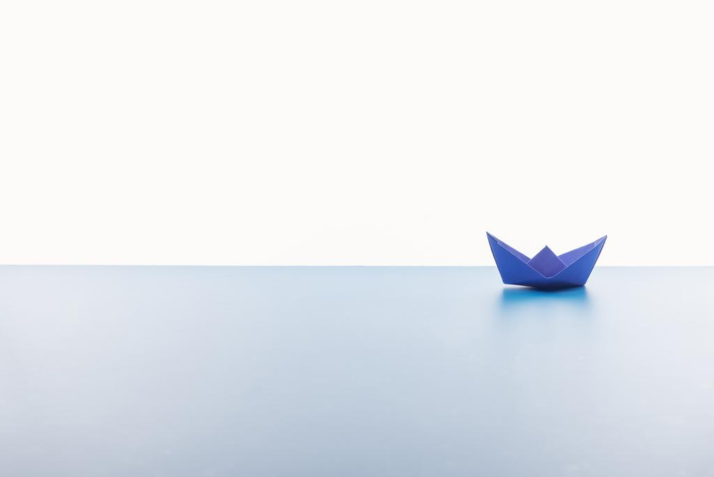 Kék papír csónak fehér háttérben fény felületén - Fotó, kép