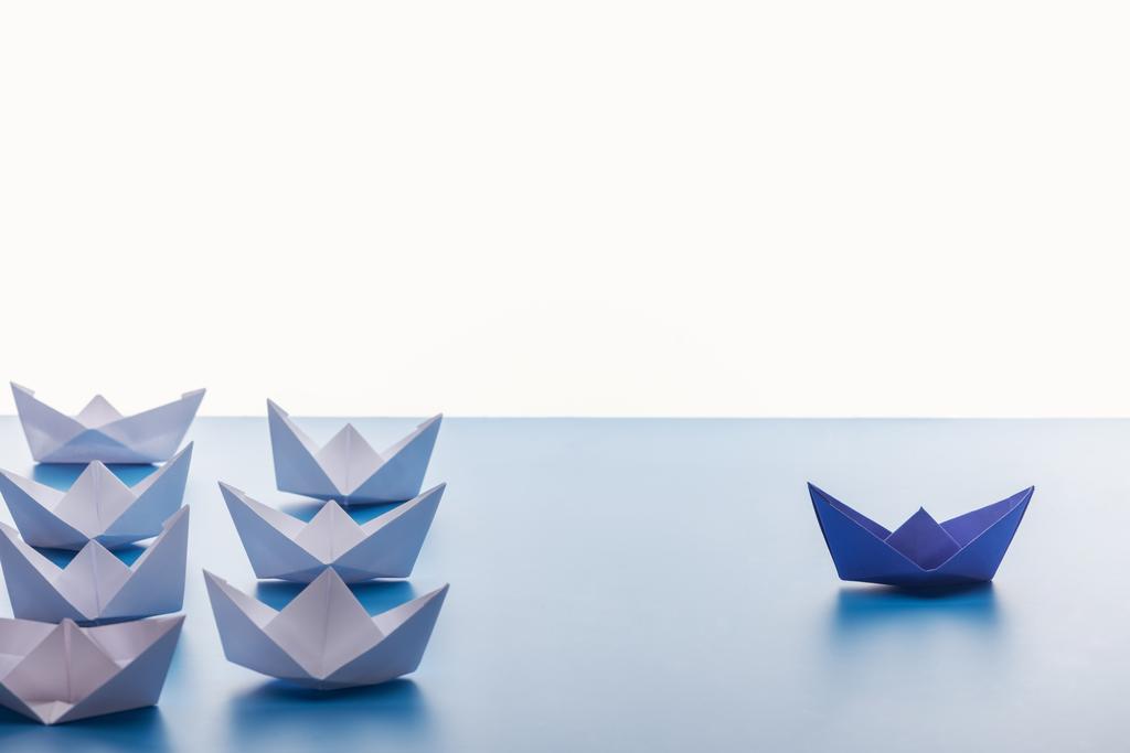 Бумажные лодки на светло-голубой поверхности на белом фоне
 - Фото, изображение