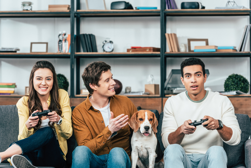 Beagle köpek tutarak joystick ve video oyunları oynarken ile üç çok ırklı arkadaşlar - Fotoğraf, Görsel