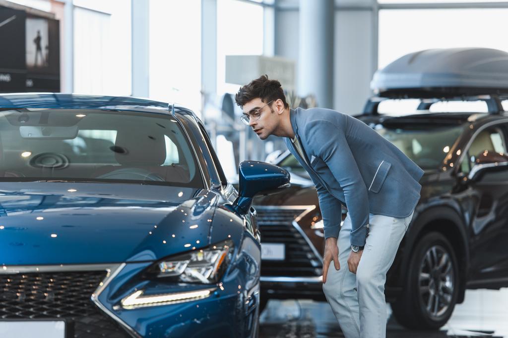 uomo elegante in occhiali guardando l'automobile mentre in piedi in showroom auto
  - Foto, immagini