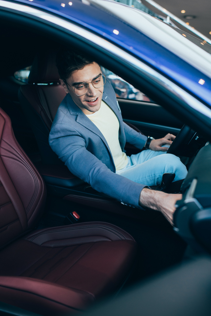 Selektiver Fokus des erfolgreichen fröhlichen Mannes mit Brille, der im Auto sitzt  - Foto, Bild