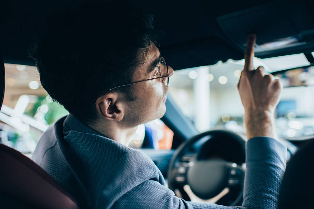 selectieve focus van succesvolle man in glazen gesturing zittend in de auto  - Foto, afbeelding