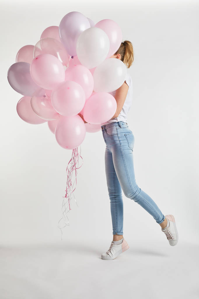 дівчина в повсякденному одязі, що покриває обличчя рожевими повітряними кульками на білому
 - Фото, зображення