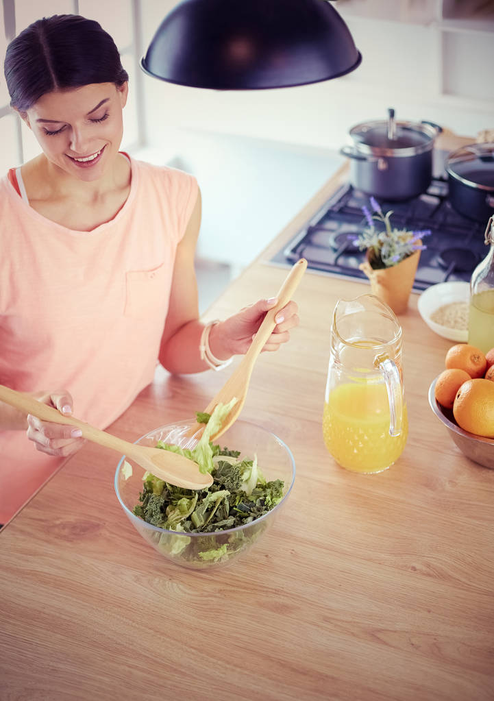 glimlachende jonge vrouw mengen van verse salade in de keuken. - Foto, afbeelding