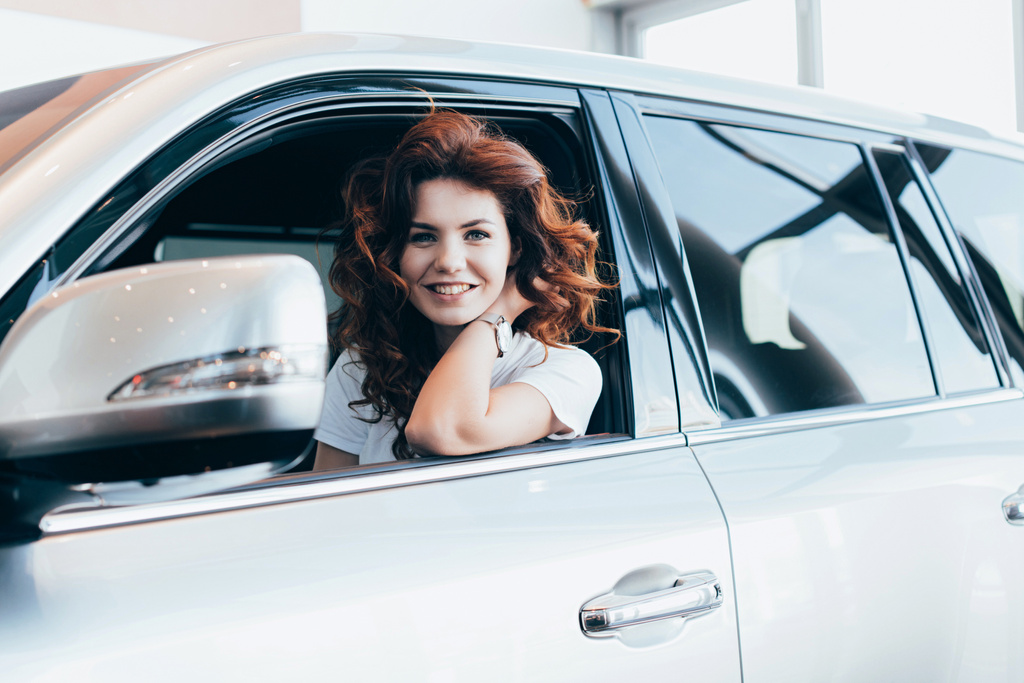 Otomobil otururken gülümseyen neşeli kıvırcık kadın seçici odak  - Fotoğraf, Görsel