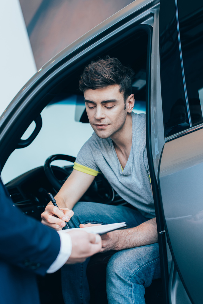 bijgesneden weergave van auto dealerbedrijf Klembord terwijl knappe man ondertekening contract - Foto, afbeelding