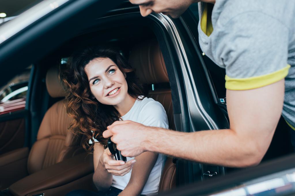 enfoque selectivo del hombre dando las llaves a la mujer atractiva que se sienta en automóvil
  - Foto, Imagen