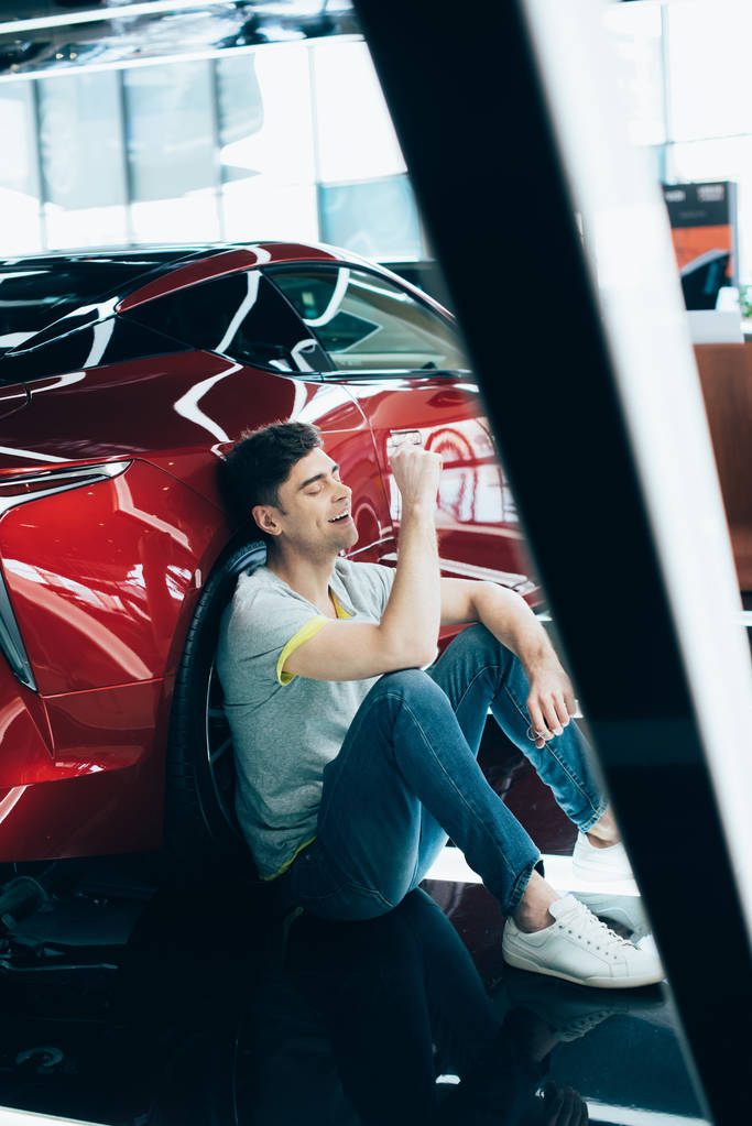 foco seletivo de homem feliz sentado e rindo perto de carro vermelho
  - Foto, Imagem