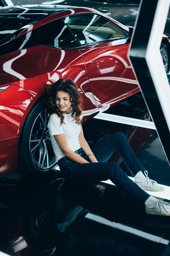 вибірковий фокус щасливої жінки, що сидить на підлозі біля нової червоної машини
 - Фото, зображення