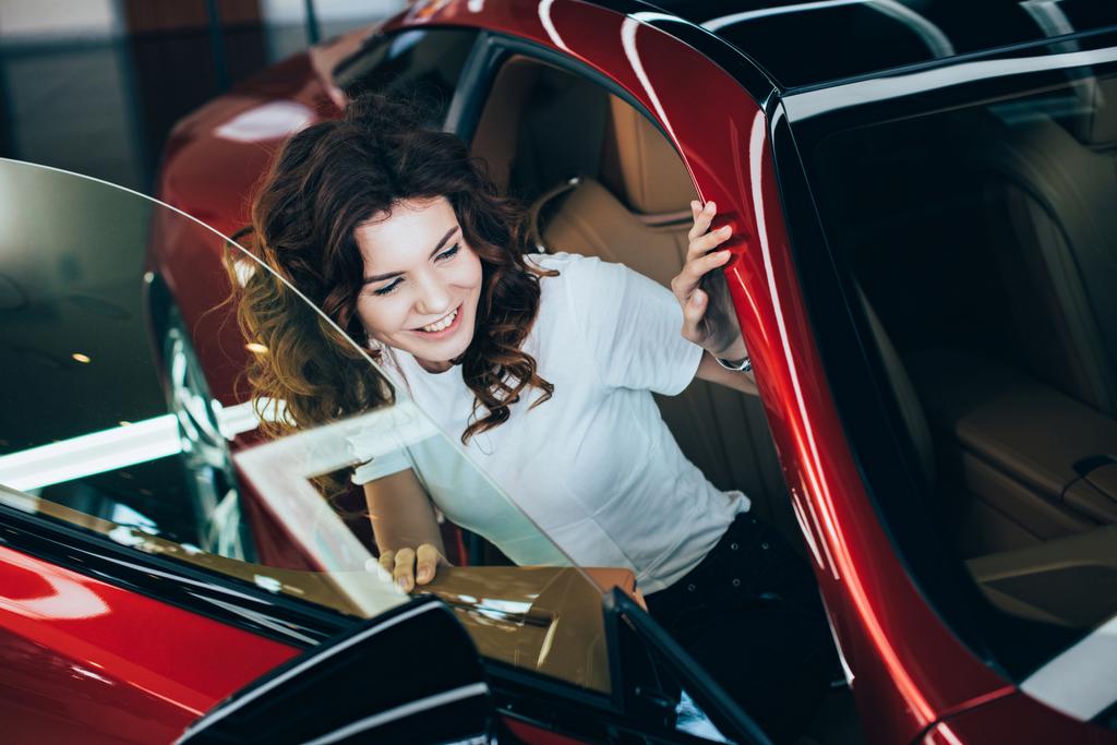 selektywne skupienie uśmiechnięta ładna kobieta siedzi w nowym czerwonym samochodzie - Zdjęcie, obraz