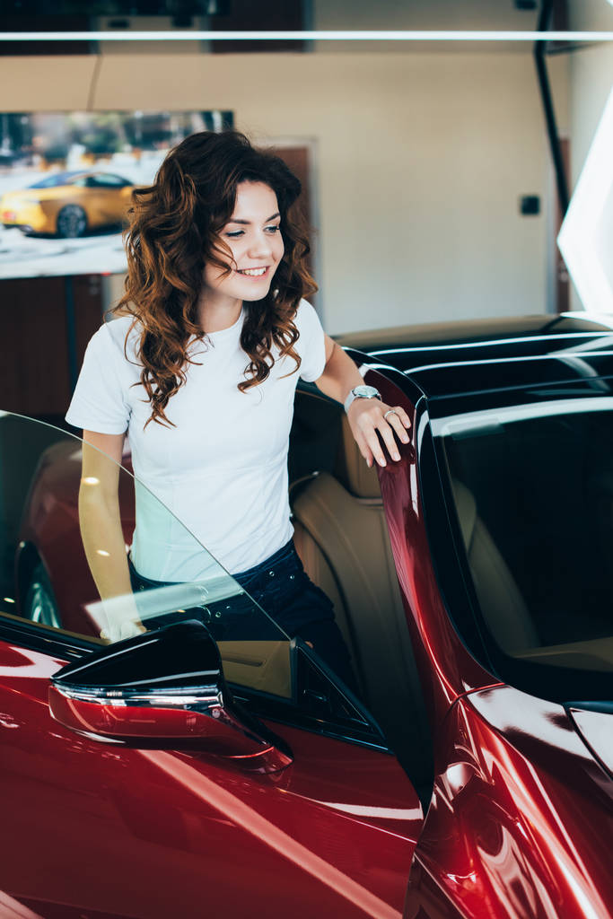 όμορφη ευτυχισμένη γυναίκα που στέκεται νέο νέο κόκκινο αυτοκίνητο σε εκθεσιακός χώρος - Φωτογραφία, εικόνα