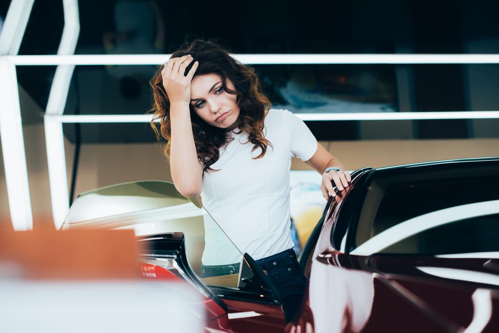 selectieve focus van vermoeide vrouw staande in de buurt van auto in auto showroom - Foto, afbeelding