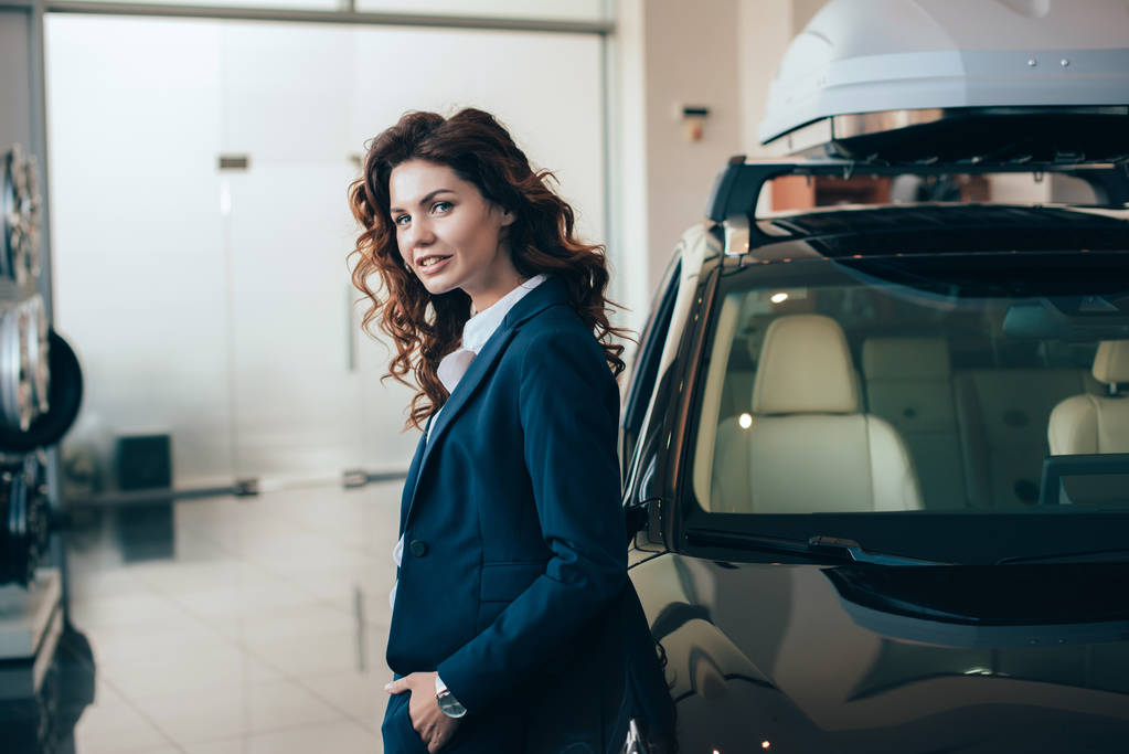 beautiful businesswoman standing near car and holding hand in pocket - Photo, Image