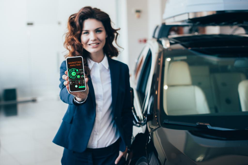 enfoque selectivo de la mujer de negocios bonita mostrando teléfono inteligente con gráficos y gráficos en la pantalla y de la mano en el bolsillo
 - Foto, imagen
