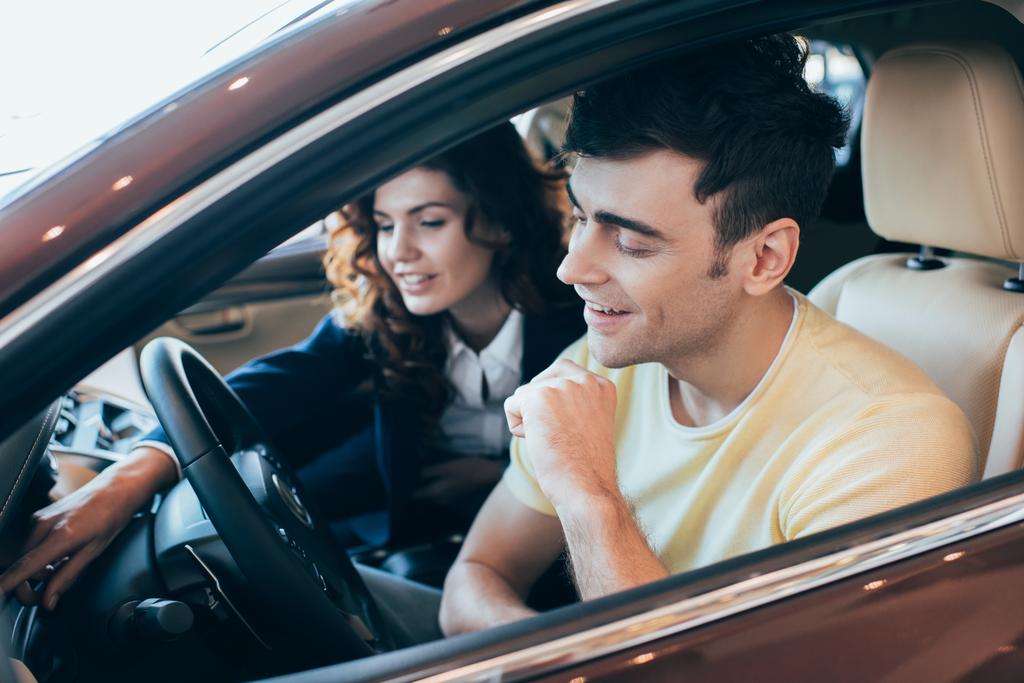 селективный фокус улыбающегося автодилера и клиента, сидящего вместе в новом автомобиле
 - Фото, изображение
