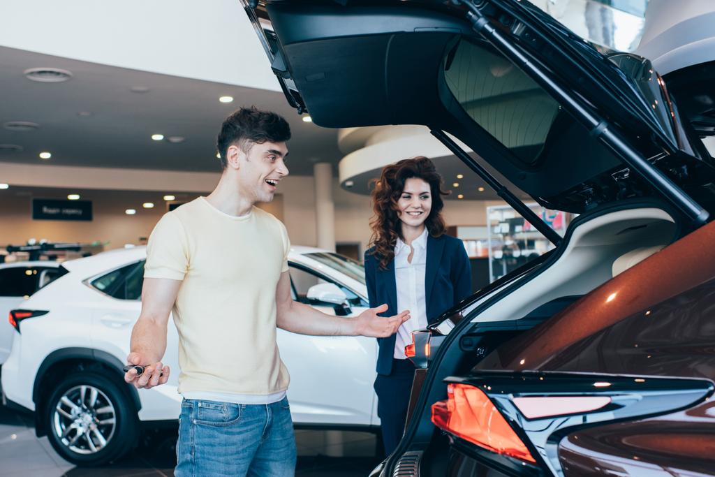selective focus of smiling car dealer and happy customer standing near new car  - Photo, Image