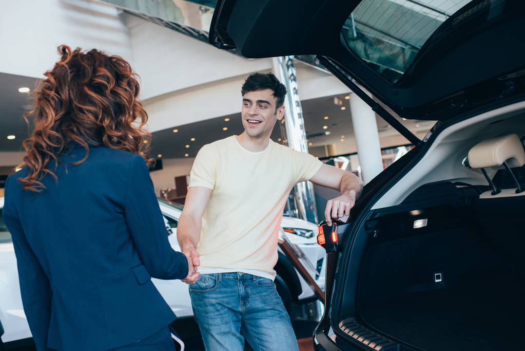 foco seletivo de homem feliz e negociante de carro apertando as mãos no showroom do carro
 - Foto, Imagem