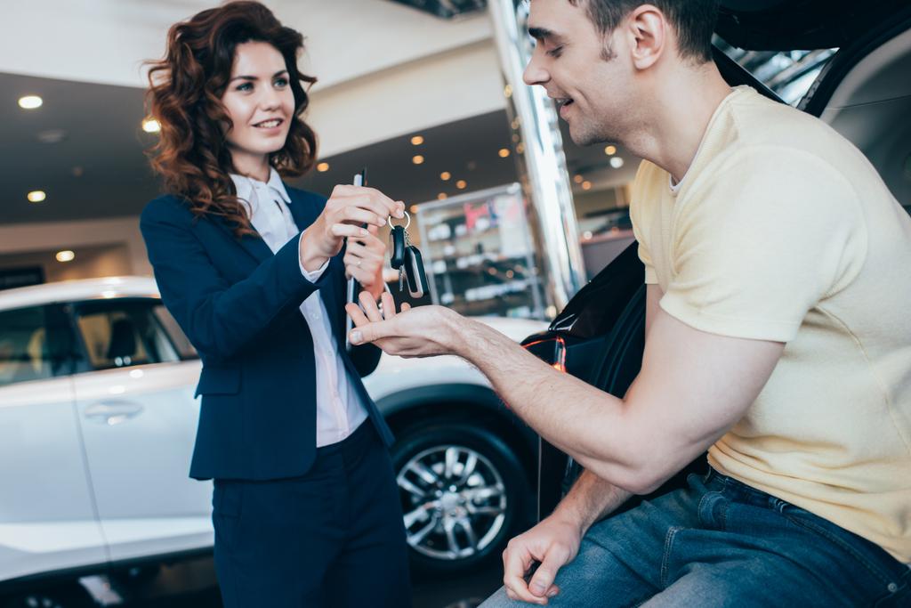 selektivní zaměření obchodníka s autem s úsměvem, který dává klíčky od auta šťastným klientům - Fotografie, Obrázek