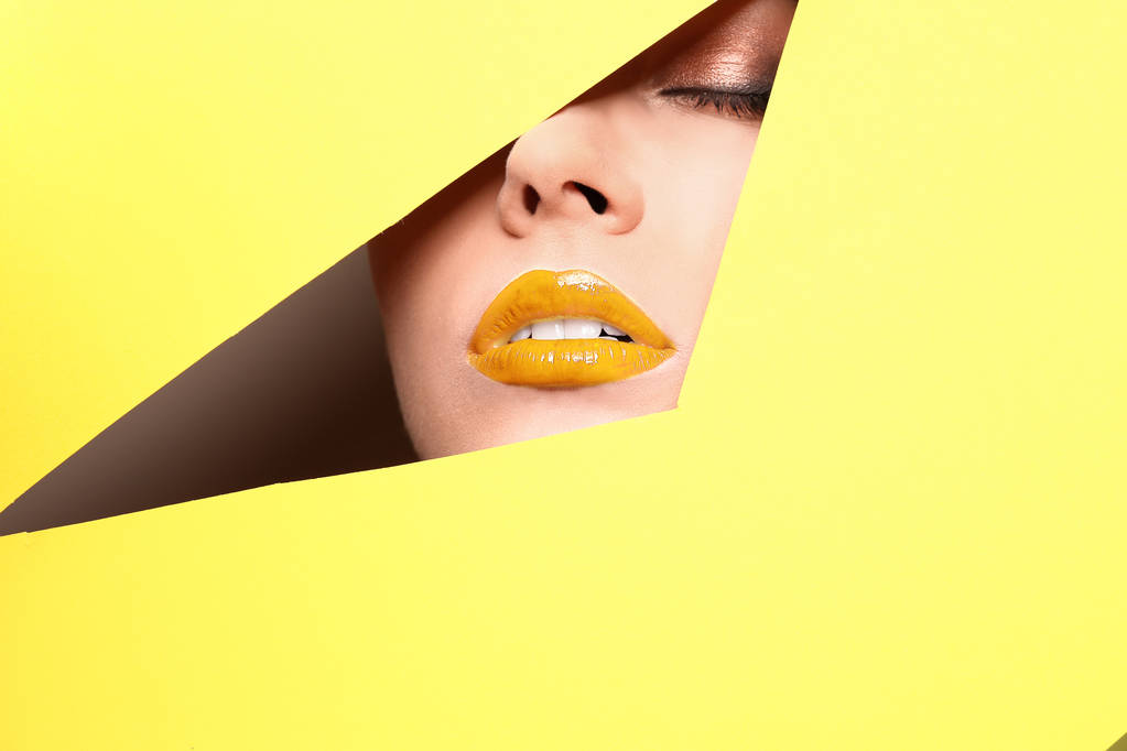 Vista de la hermosa mujer joven con labios de oro a través de recorte en papel de color, primer plano
 - Foto, Imagen