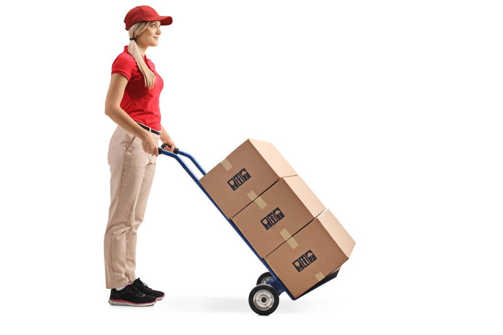 Volledige lengte shot van een vrouwelijke werknemer permanent met dozen op een hand vrachtwagen geïsoleerd op witte achtergrond - Foto, afbeelding