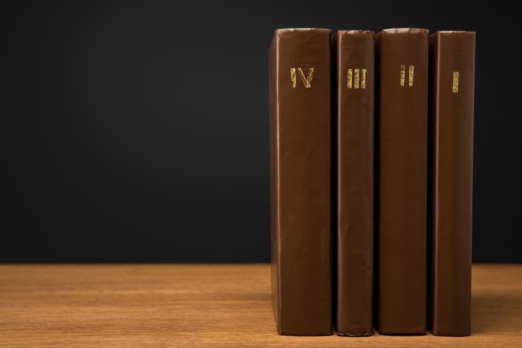 volúmenes de libros antiguos en cuero cubiertas marrones sobre mesa de madera aislada en negro
 - Foto, Imagen