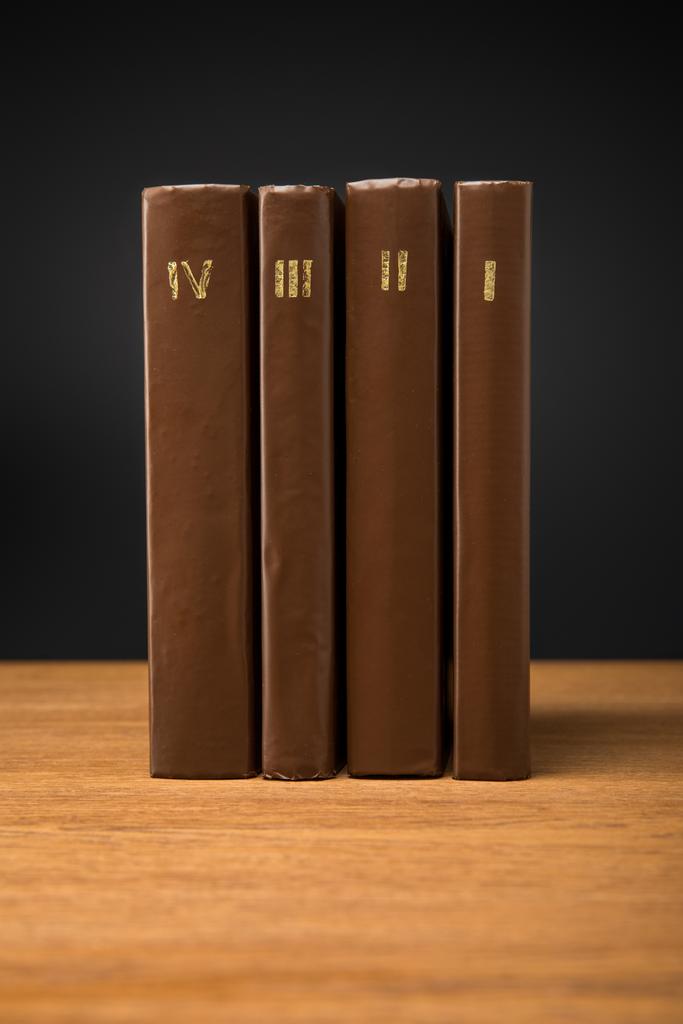 volumes of retro books in leather brown covers on wooden table isolated on black - Photo, Image