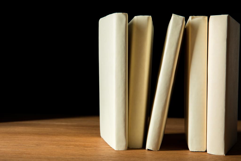 rij van boeken in witte covers op houten tafel geïsoleerd op zwart - Foto, afbeelding