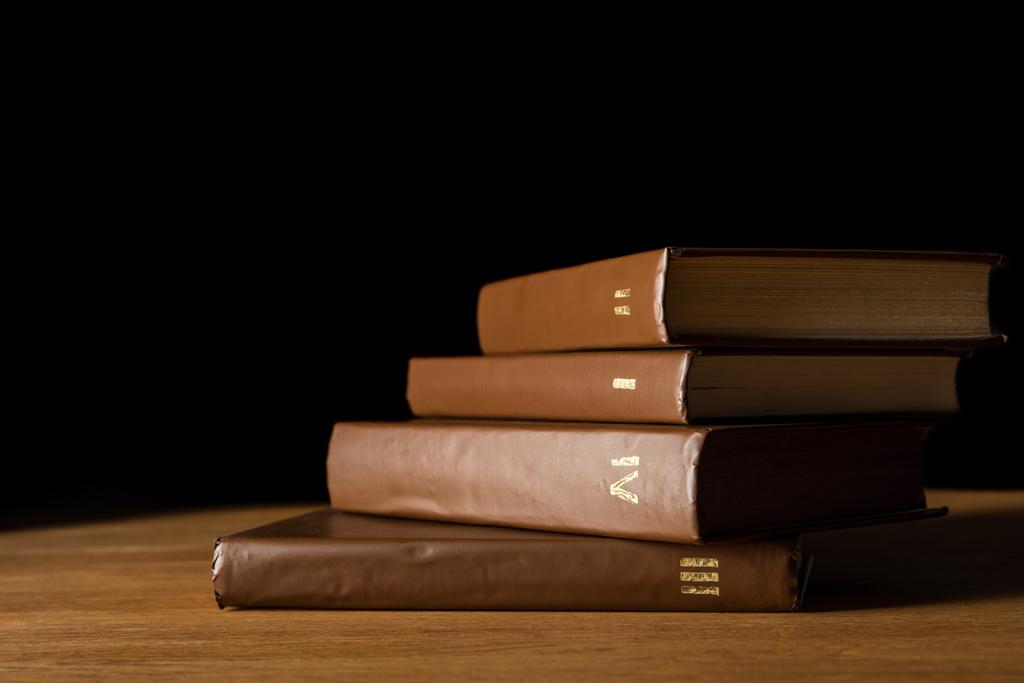 επιλεκτική εστίαση από καφέ δέρμα βιβλία σχετικά με ξύλινο τραπέζι που απομονώνονται σε μαύρο - Φωτογραφία, εικόνα