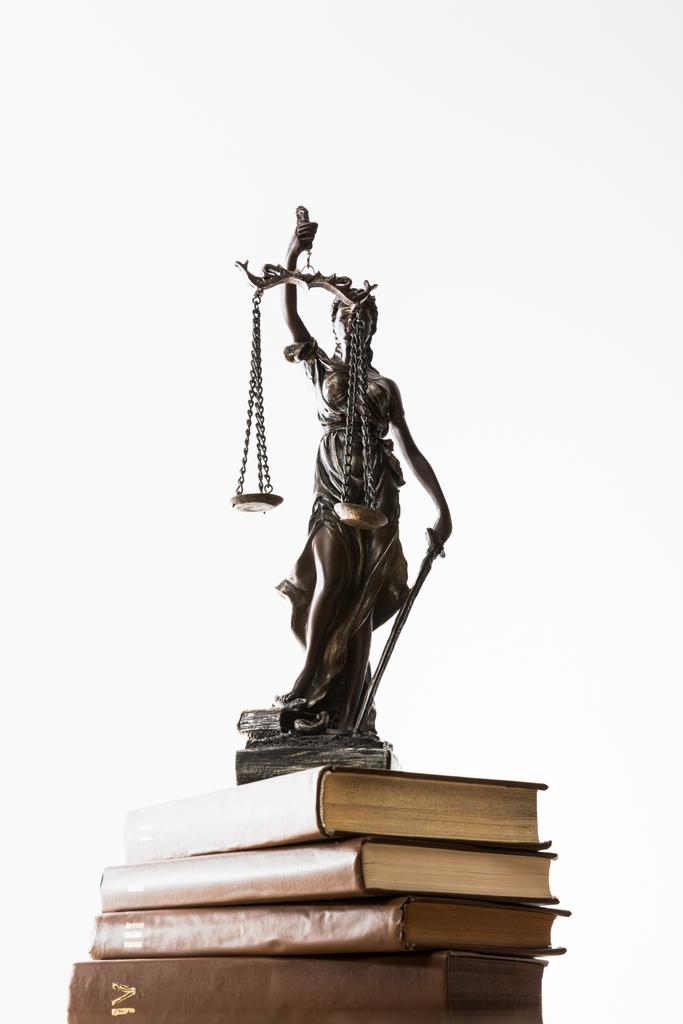 low angle view of bronze figurine with scales of justice on pile of brown books isolated on white - Photo, Image