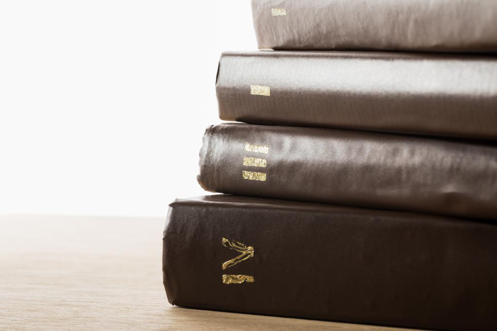 Bände alter Bücher in lederbraunen Einbänden auf Holztisch isoliert auf weißem Hintergrund - Foto, Bild
