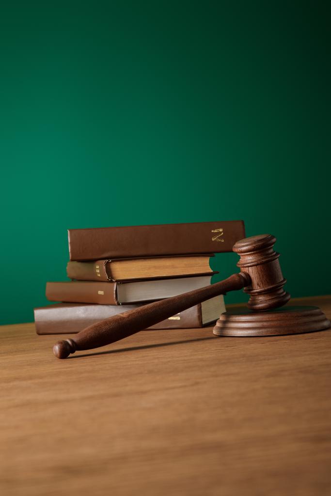 volumes of brown books in leather covers and gavel on wooden table on dark green background - Photo, Image