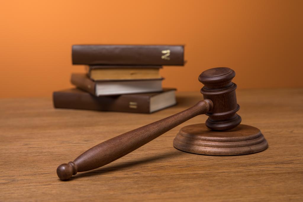 selective focus of volumes of brown books in leather covers and wooden gavel on table on orange background - Photo, Image