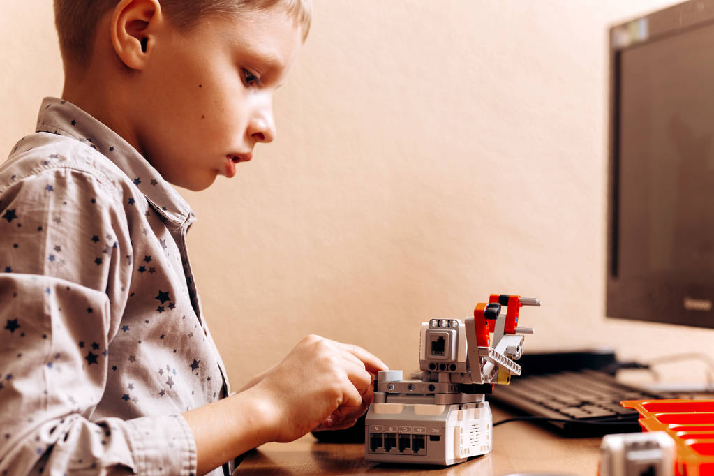 Okos fiú öltözött, szürke póló teszi a robot a robot kivitelező az íróasztalnál számítógép a robotika iskola - Fotó, kép