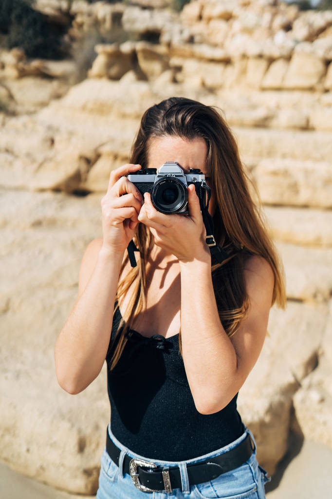 Привлекательная молодая женщина делает фотографии на своей винтажной камере на пляже во время летних каникул - Фото, изображение