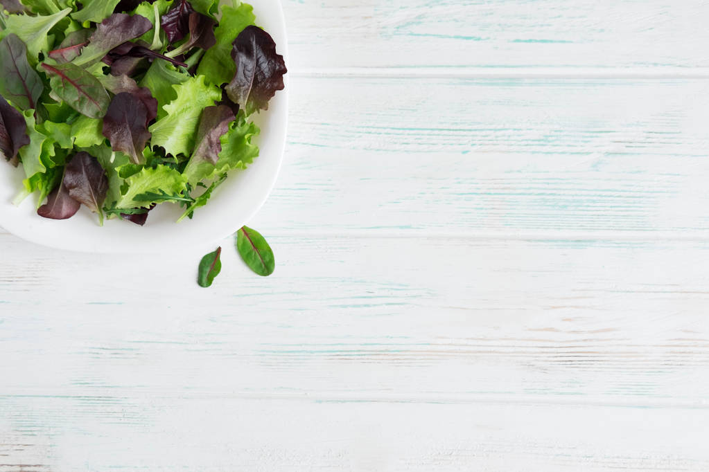 Tányér saláta fehér fa háttér. Saláta zöldek. Bioélelmiszerek. Vega étel. Design egy banner, a természetes élelmiszerek. Saláta, hogy lefogy. Lapos feküdt, top view. - Fotó, kép