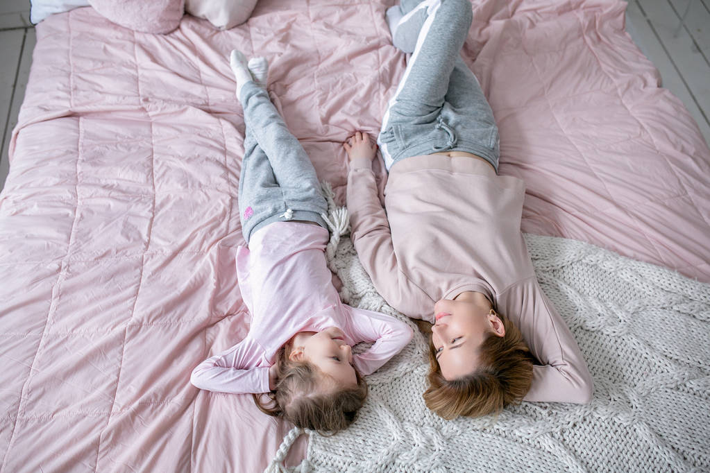 Kaunis nuori äiti ja hänen pieni tyttärensä makaavat yhdessä sängyssä makuuhuoneessa, leikkivät, halaavat ja pitävät hauskaa. Äitienhoito ja rakkaus. Vaakasuora kuva
 - Valokuva, kuva