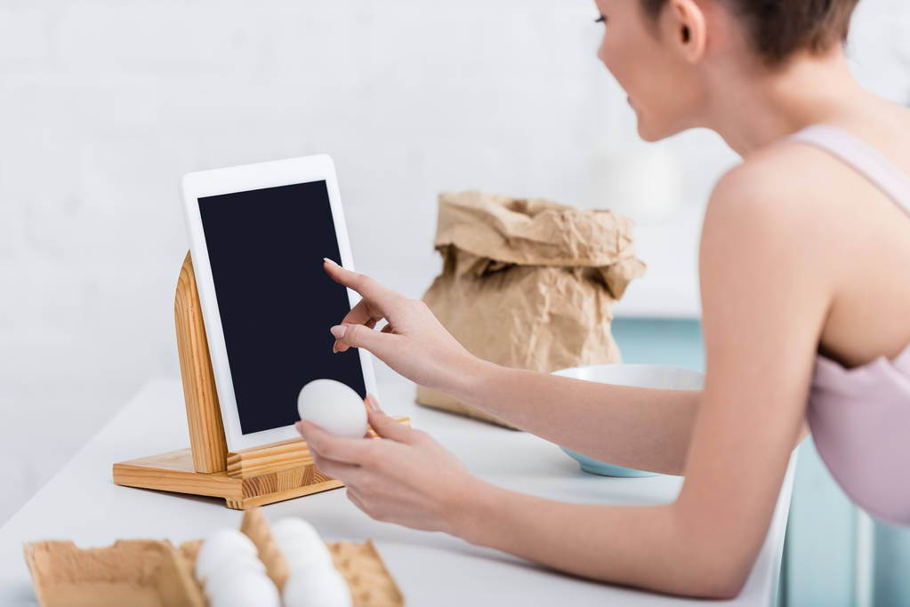 vista cortada de mulher jovem usando tablet digital com tela em branco enquanto segurando ovo
 - Foto, Imagem