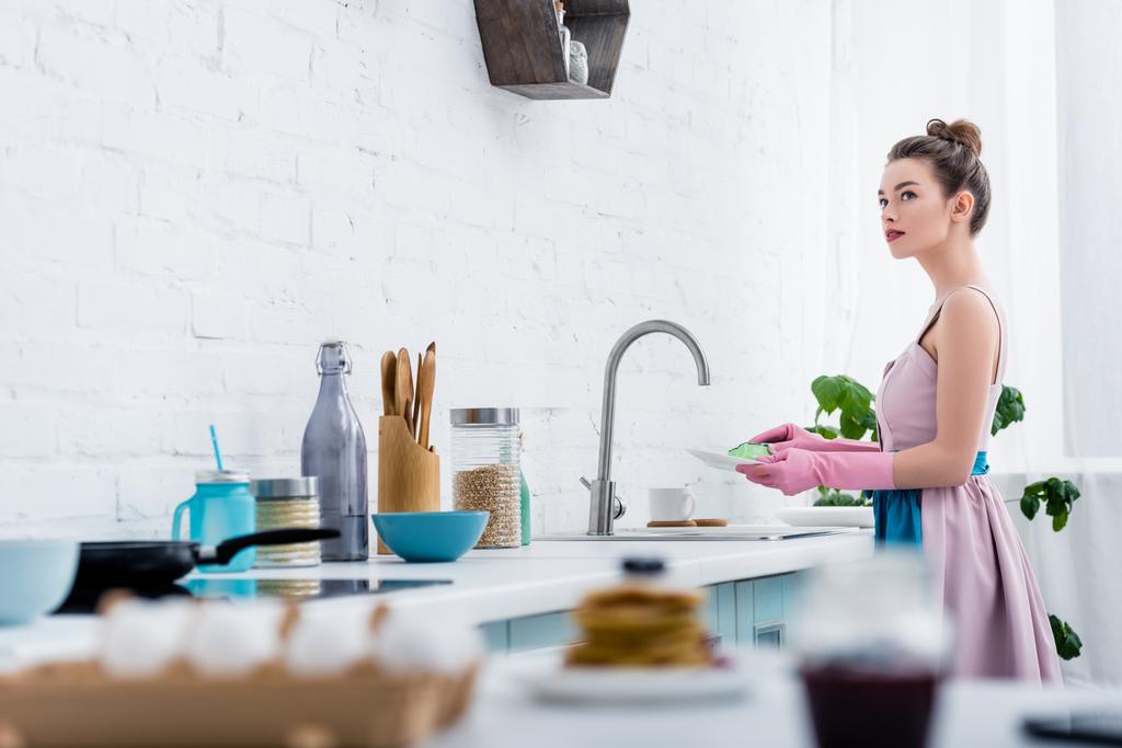 selectieve aandacht van jonge vrouw in rubberen handschoenen afwas in de keuken - Foto, afbeelding